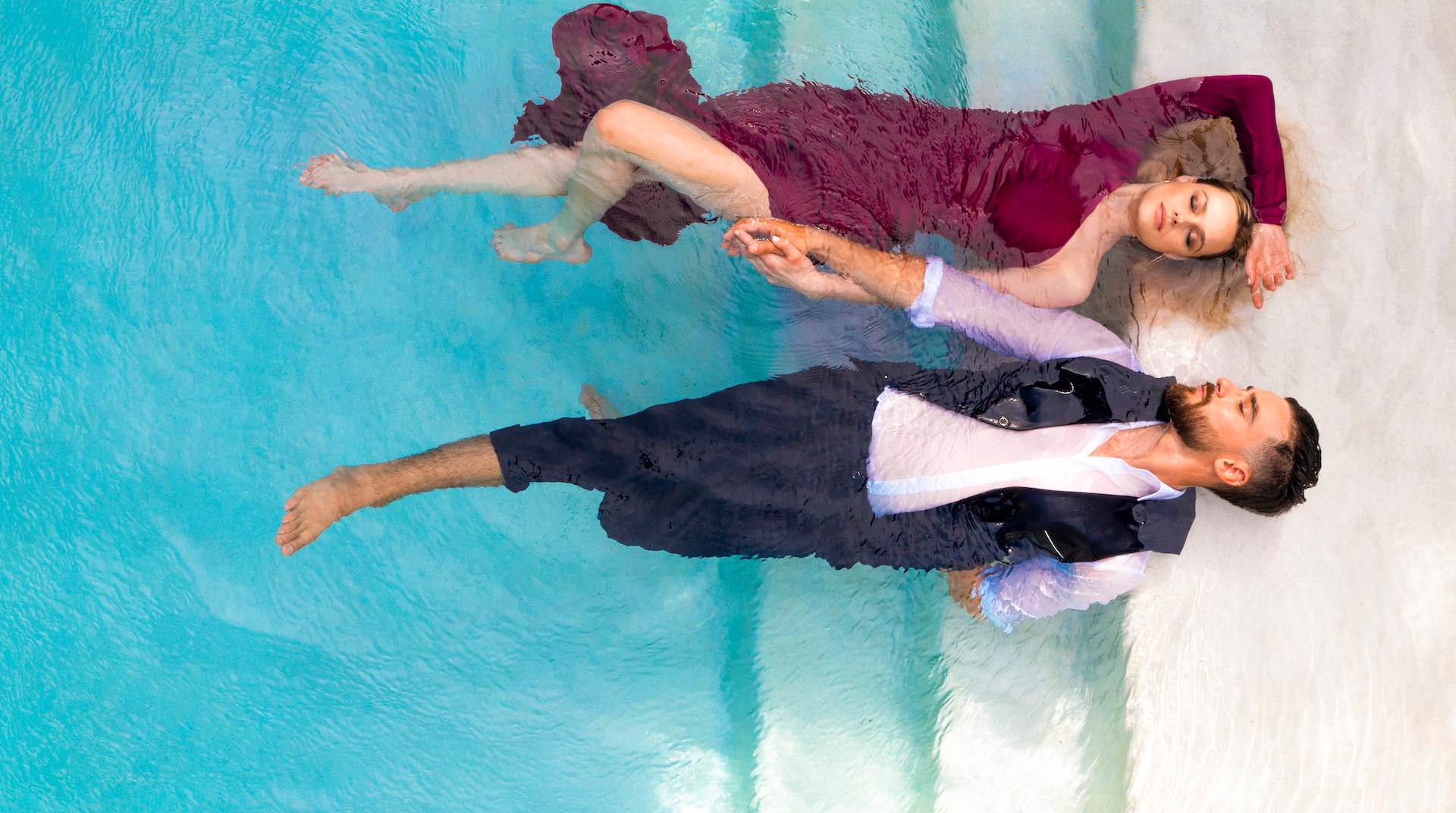 Man and women laying in pool in clothes